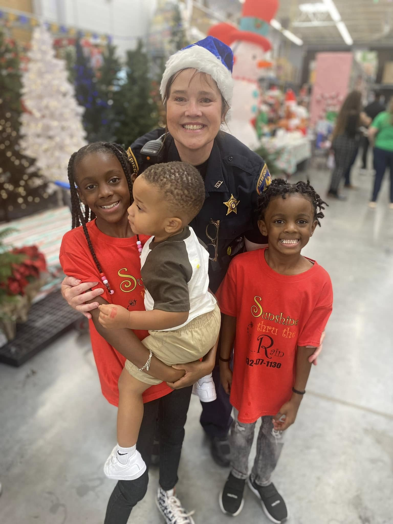 A smiling officer poses with three children during Shop With a Cop